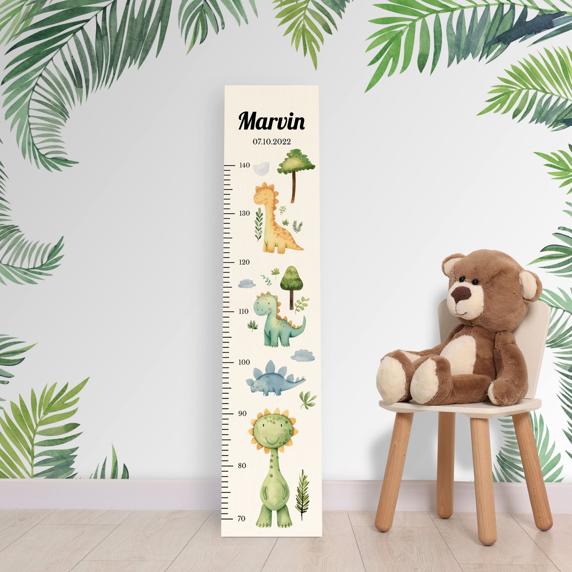 Personalisierte Messlatte aus Holz für Jungen oder Mädchen mit Dinos vor einer Kinderzimmerwand.