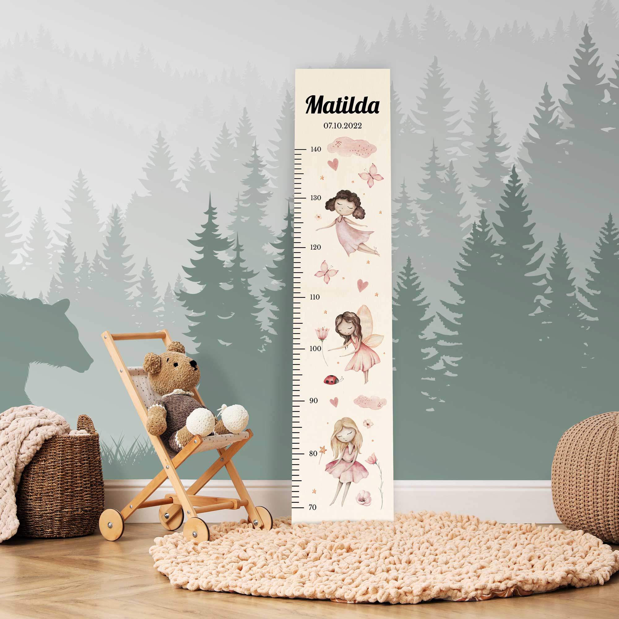 Personalisierte Messlatte aus Holz für Mädchen mit Feen vor einer Kinderzimmerwand.